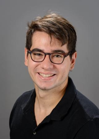 Photograph of Pedro Abelin's face. Pedro is a young Latino with brown hair. He is wearing a black shirt and brown sunglasses.