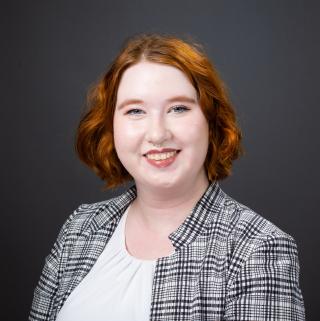White woman with orange and brown hair wearing a black and white blazer